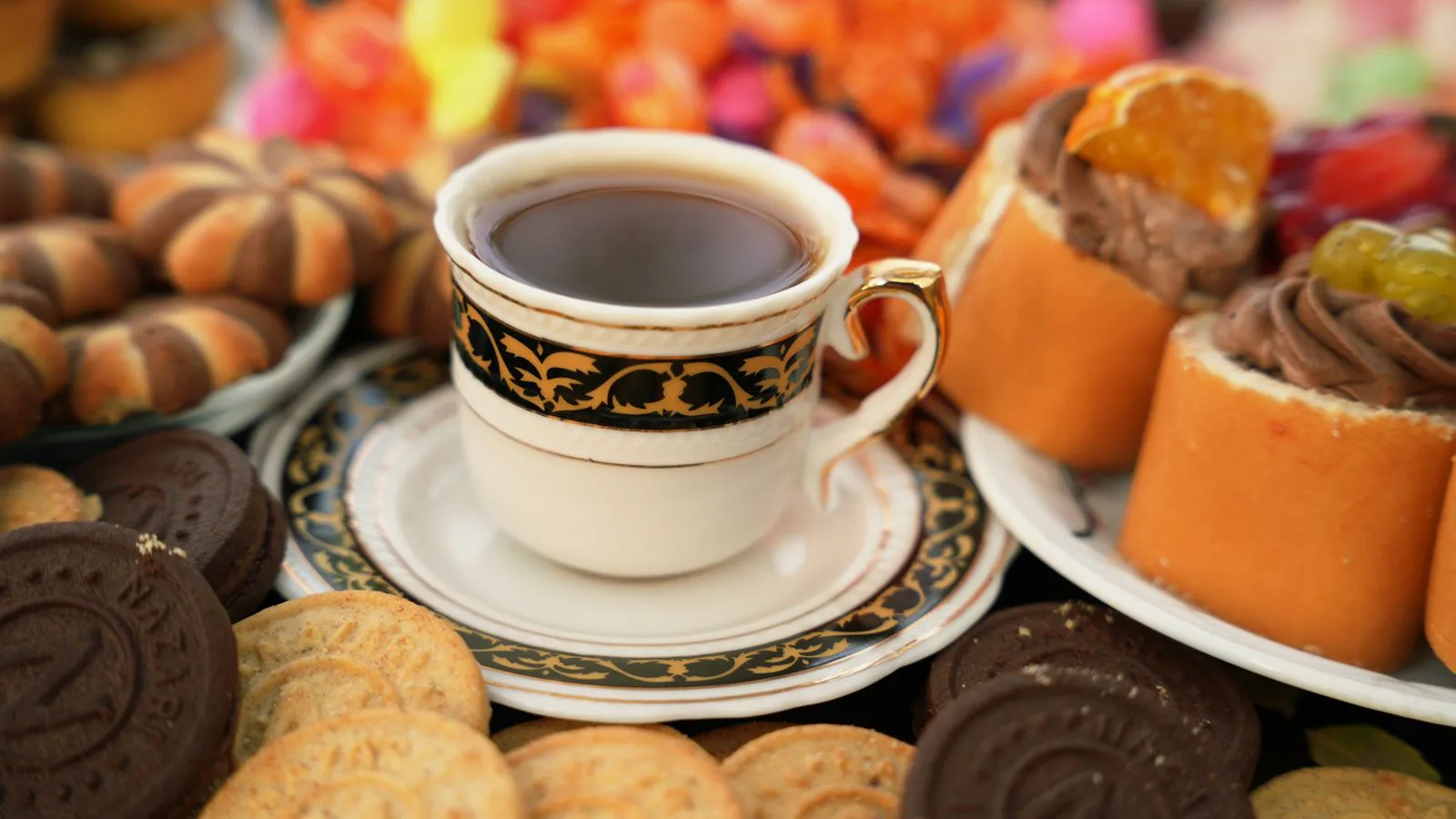 A patterned teacup and saucer surrounded by pastries.