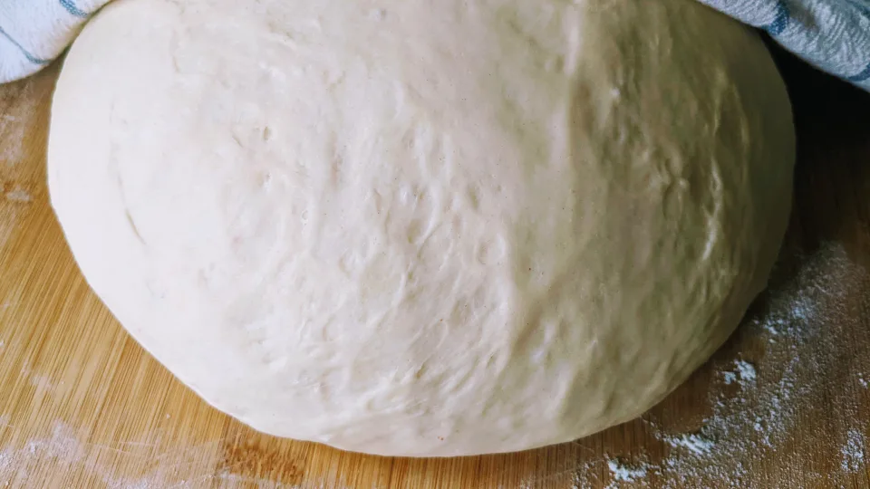 Eine aufgegangene Kugel Brotteig auf einem bemehlten Holzbrett.