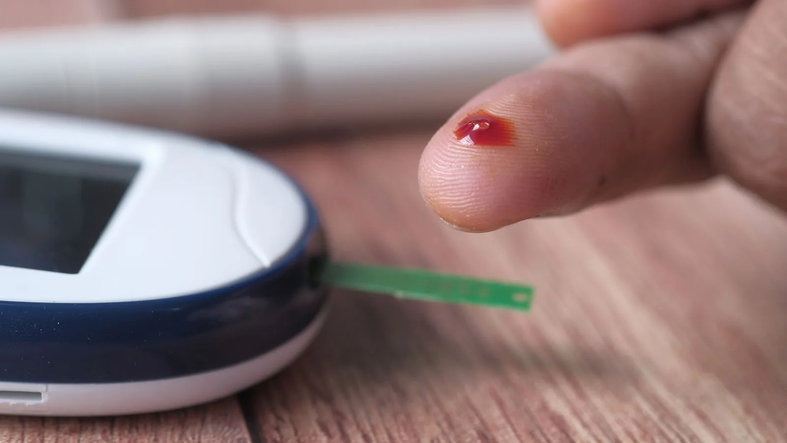 A fingertip blood drop beside a glucose meter.