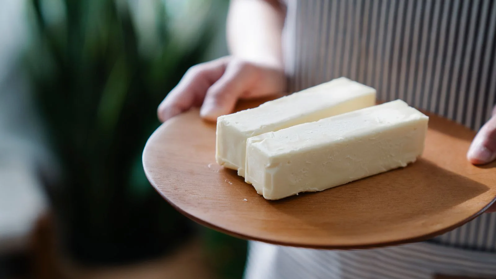 Hands holding a wooden plate with two sticks of butter.