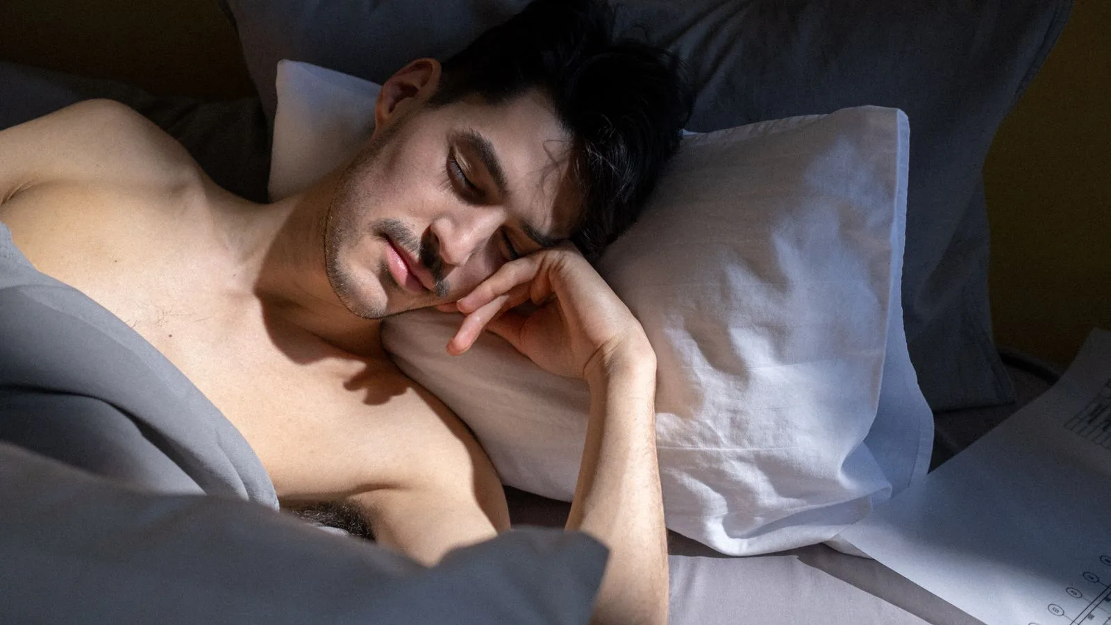 Ein Mann schläft im Bett in einem lichtdurchfluteten Zimmer.