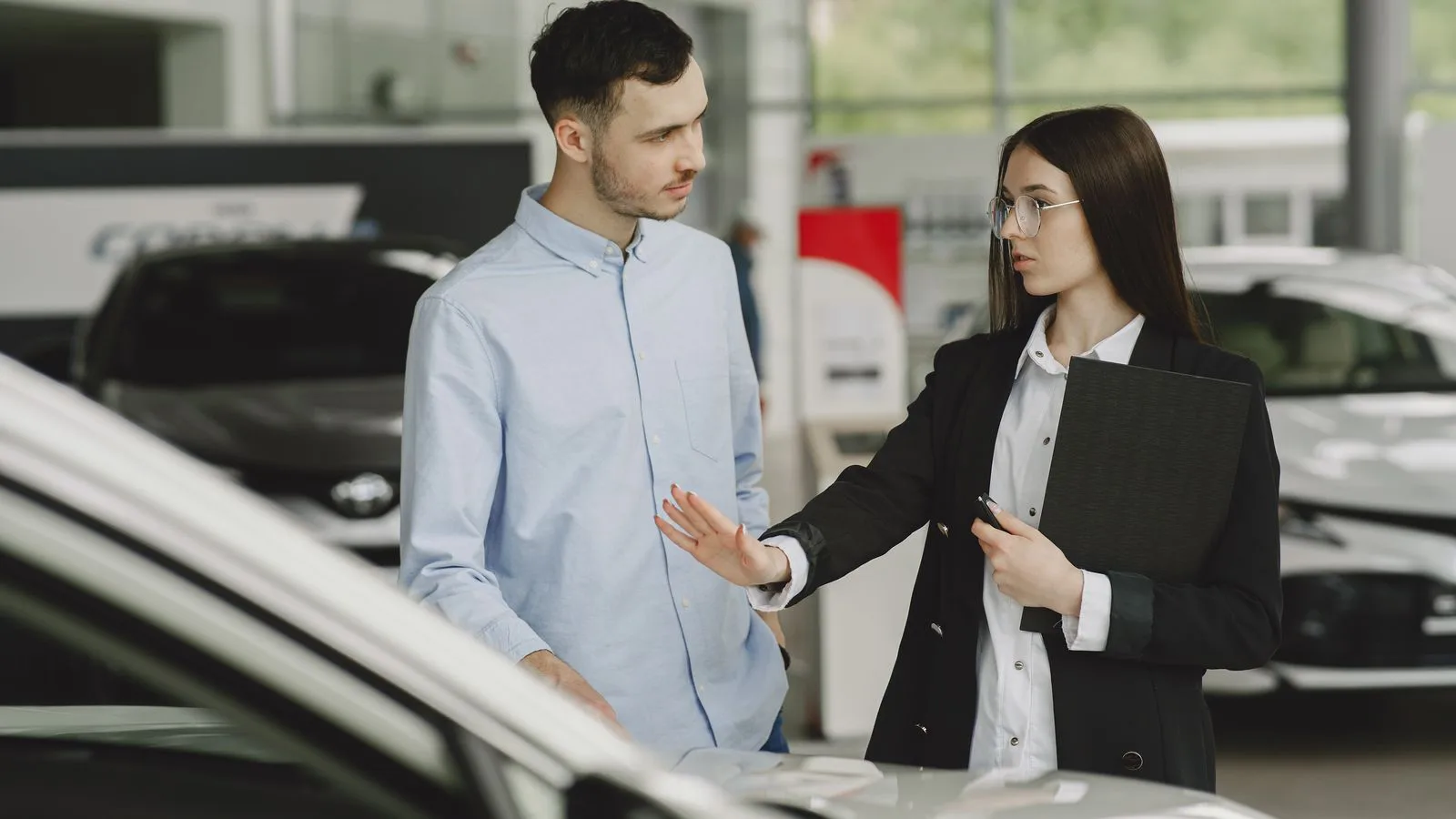 Un vendeur et une cliente discutent près d'une voiture dans un hall d'exposition.