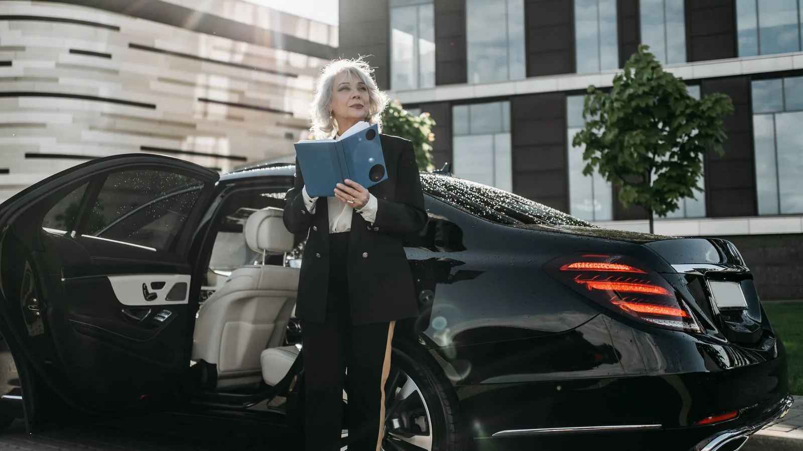 Una empresaria sale de un coche negro con documentos en la mano.