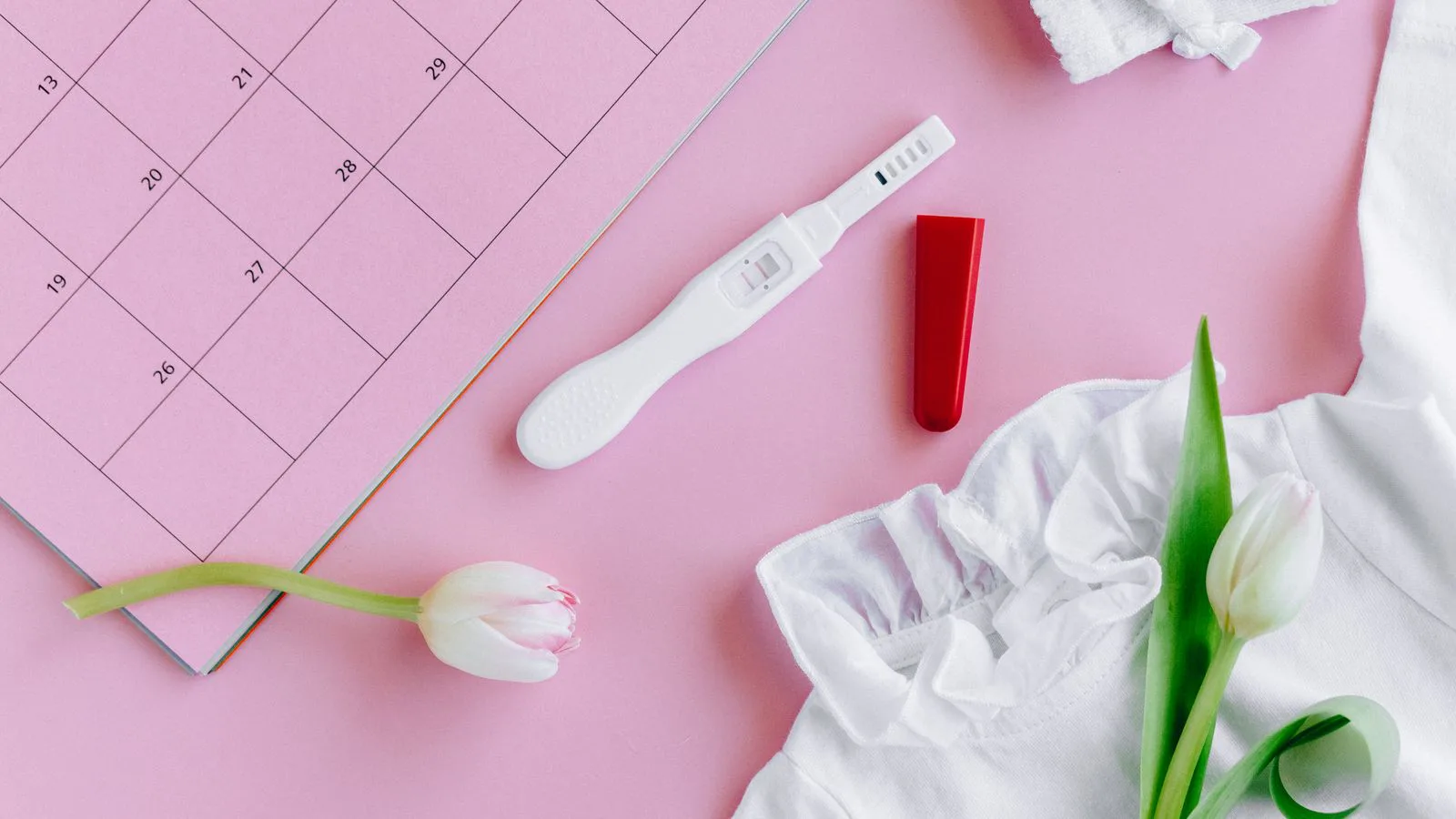 A pregnancy test and a tulip laid on a pink calendar.