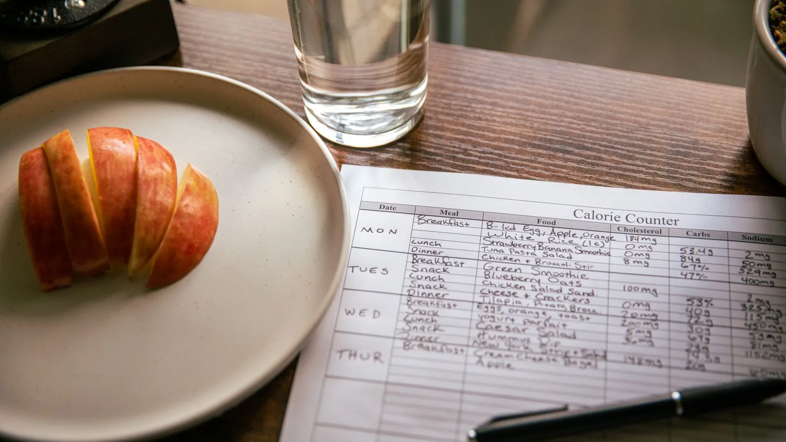 Apple slices on a plate beside a calorie-counting sheet and a glass of water.