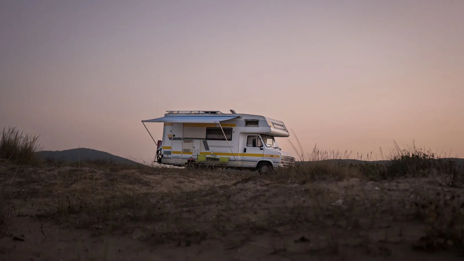A motorhome parked in open country at sunset.
