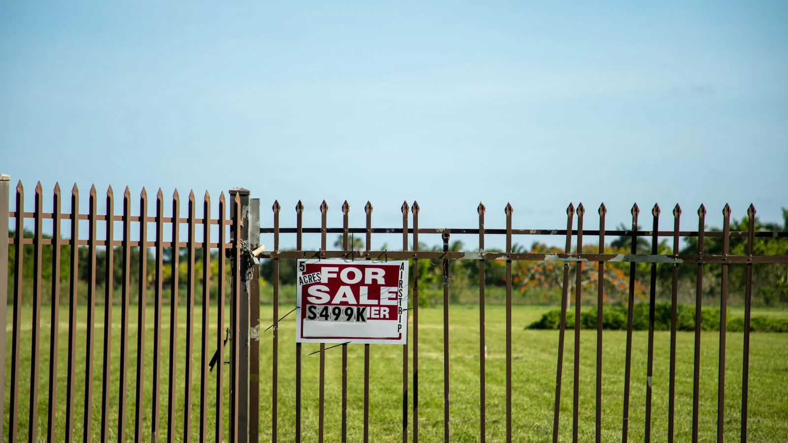 A plot of land behind an iron fence with a for-sale board.