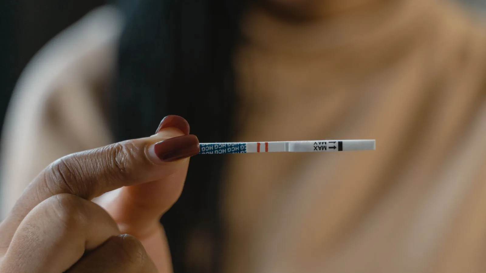 A hand holding a test strip showing two lines.