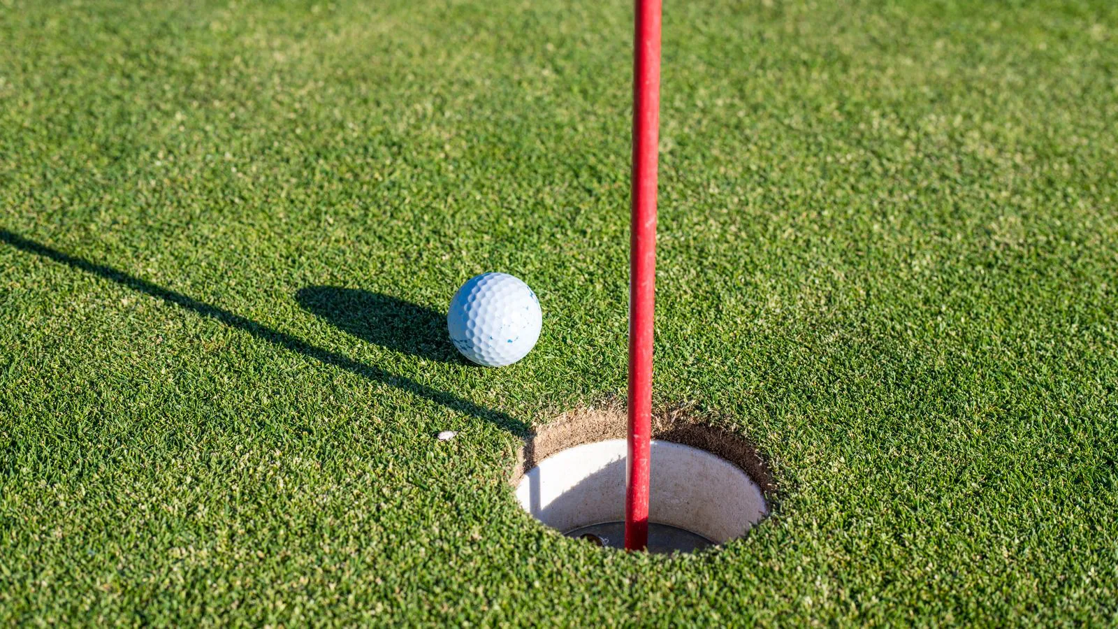 A golf ball resting beside the hole on a green, red flagstick alongside.