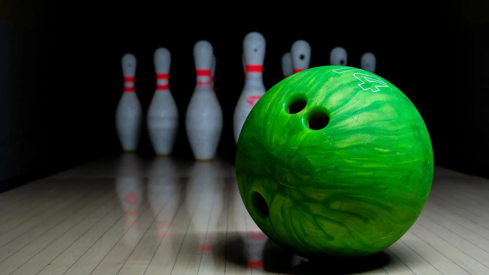 A green bowling ball on the lane with the pins standing behind.