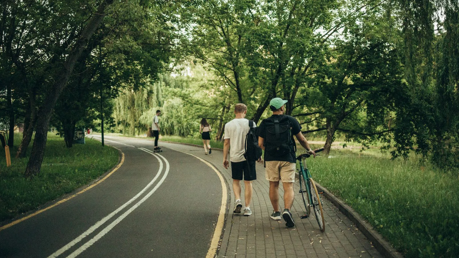 Two people walking a bicycle along a tree-lined path.