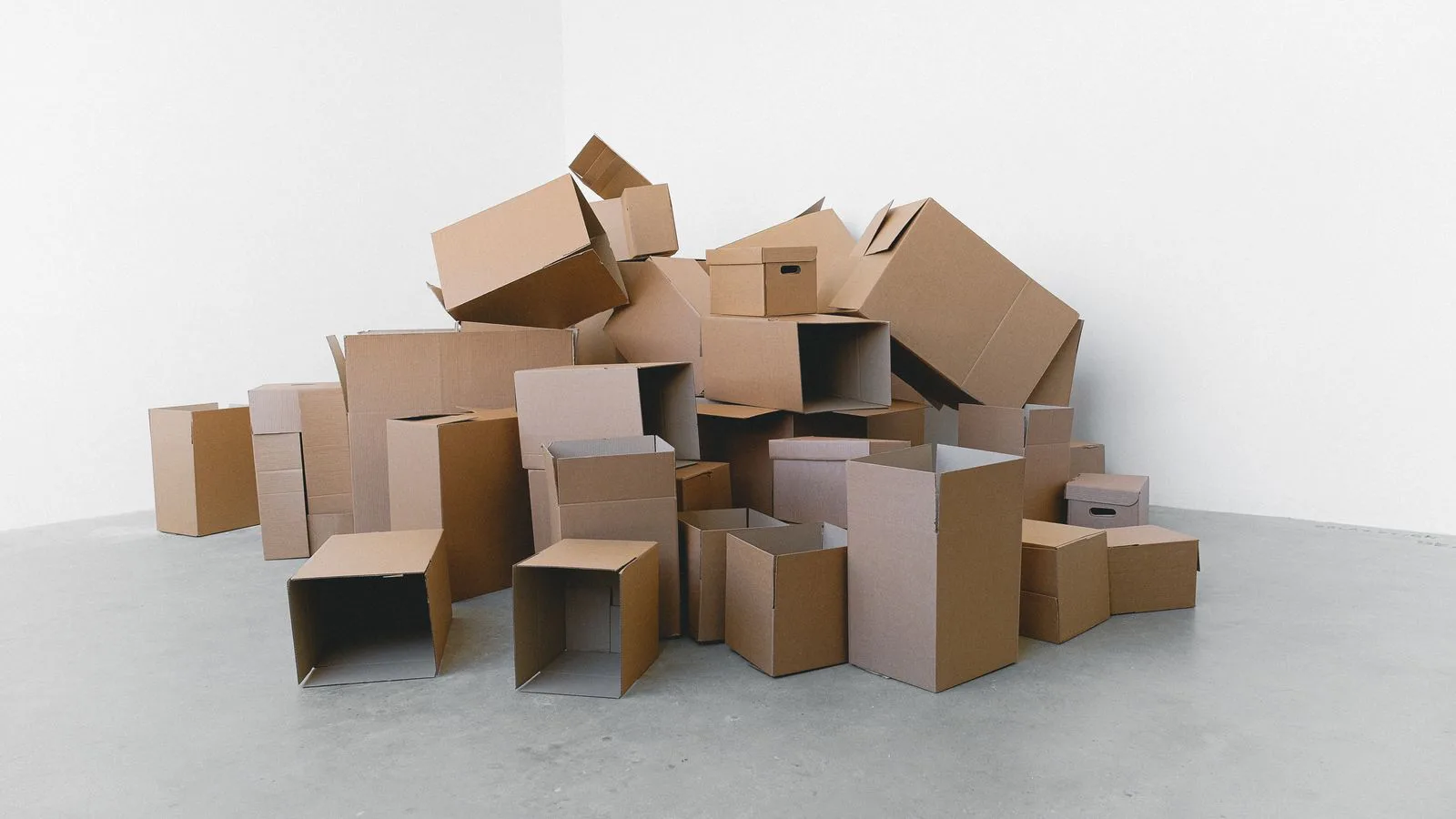 A pile of flat and folded cardboard boxes on the floor of a room.