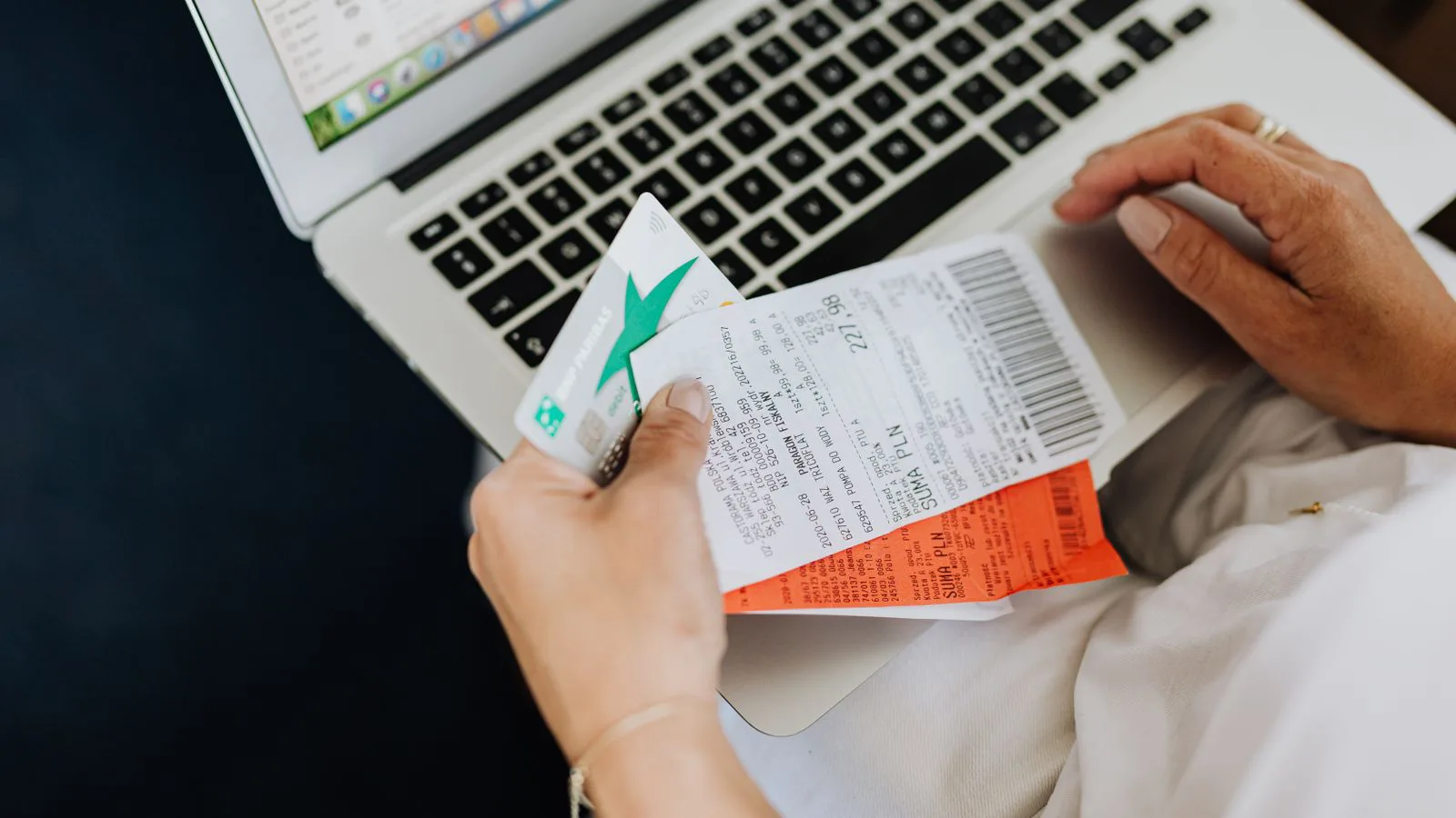Mani reggono scontrini e una carta davanti a un portatile.