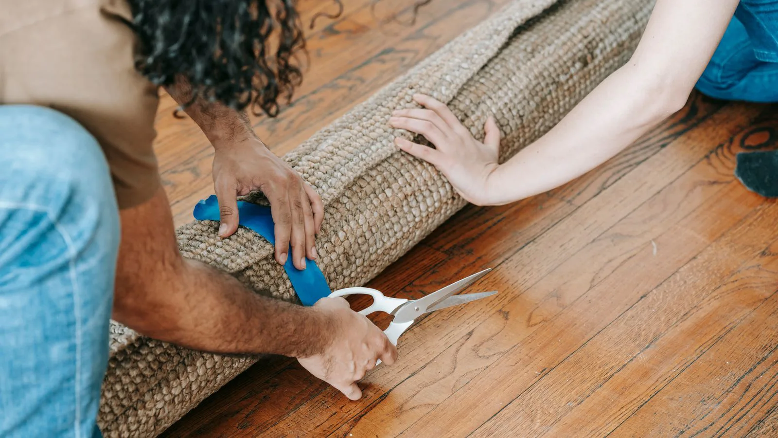 Two people rolling up a carpet on a wooden floor.