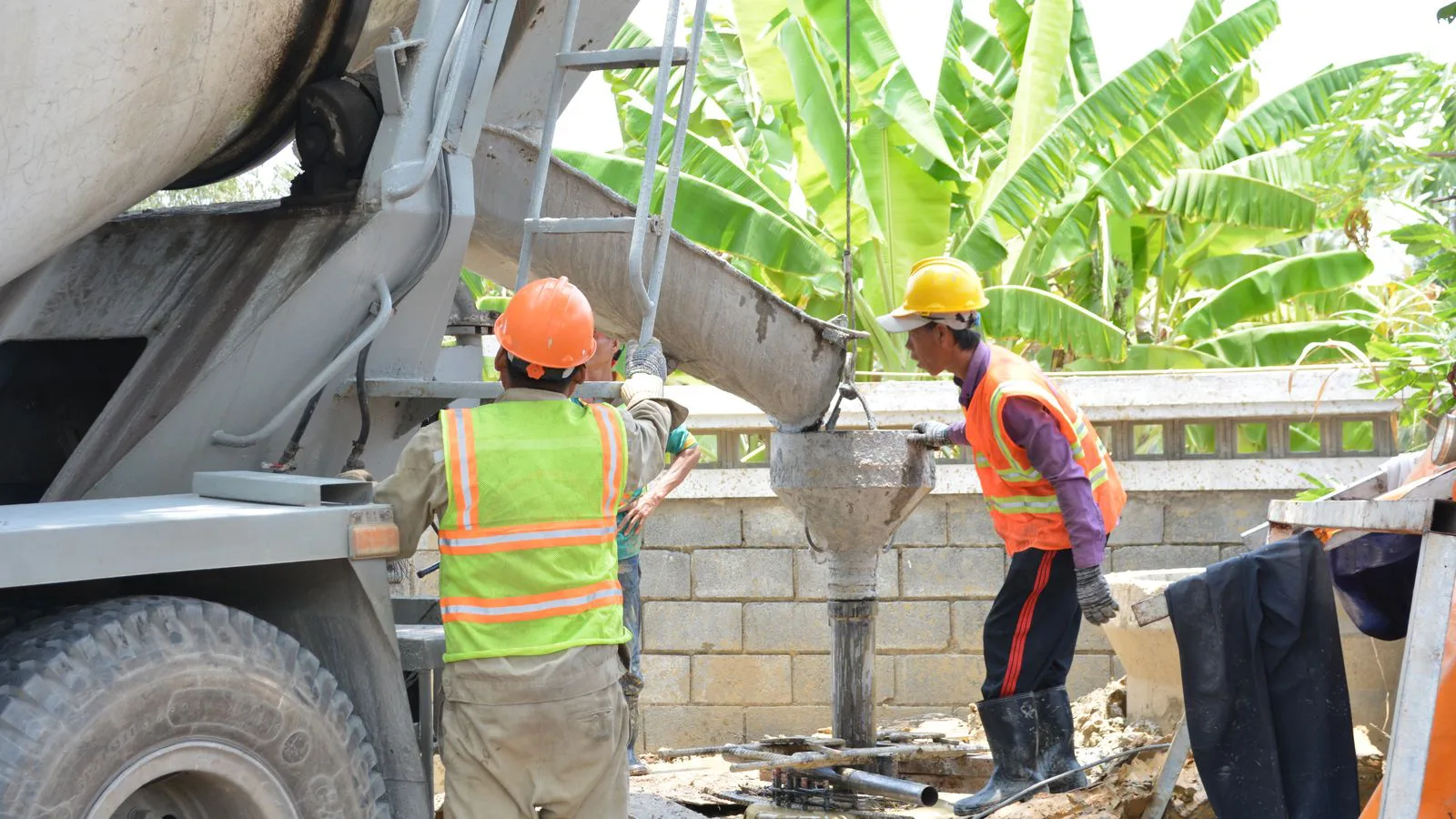 Workers pouring concrete on a site beside a mixer truck.