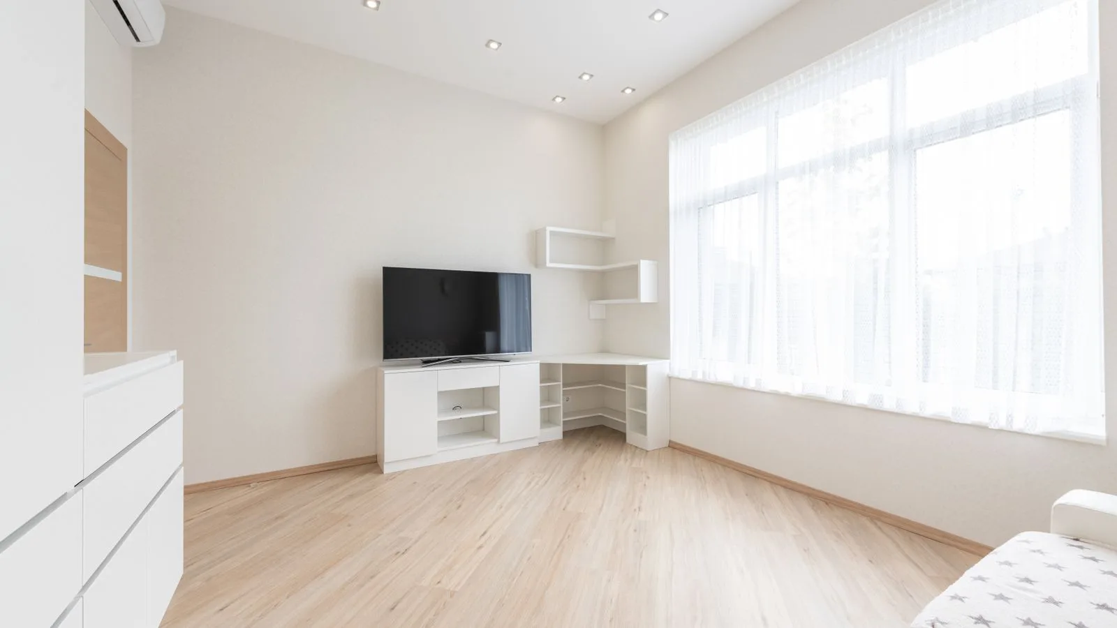 A bare room with laminate flooring and a television on a low unit.