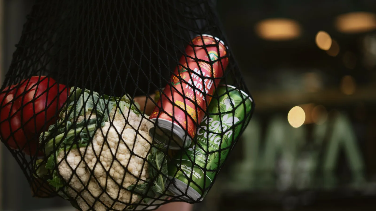 A mesh shopping bag holding vegetables and canned drinks.