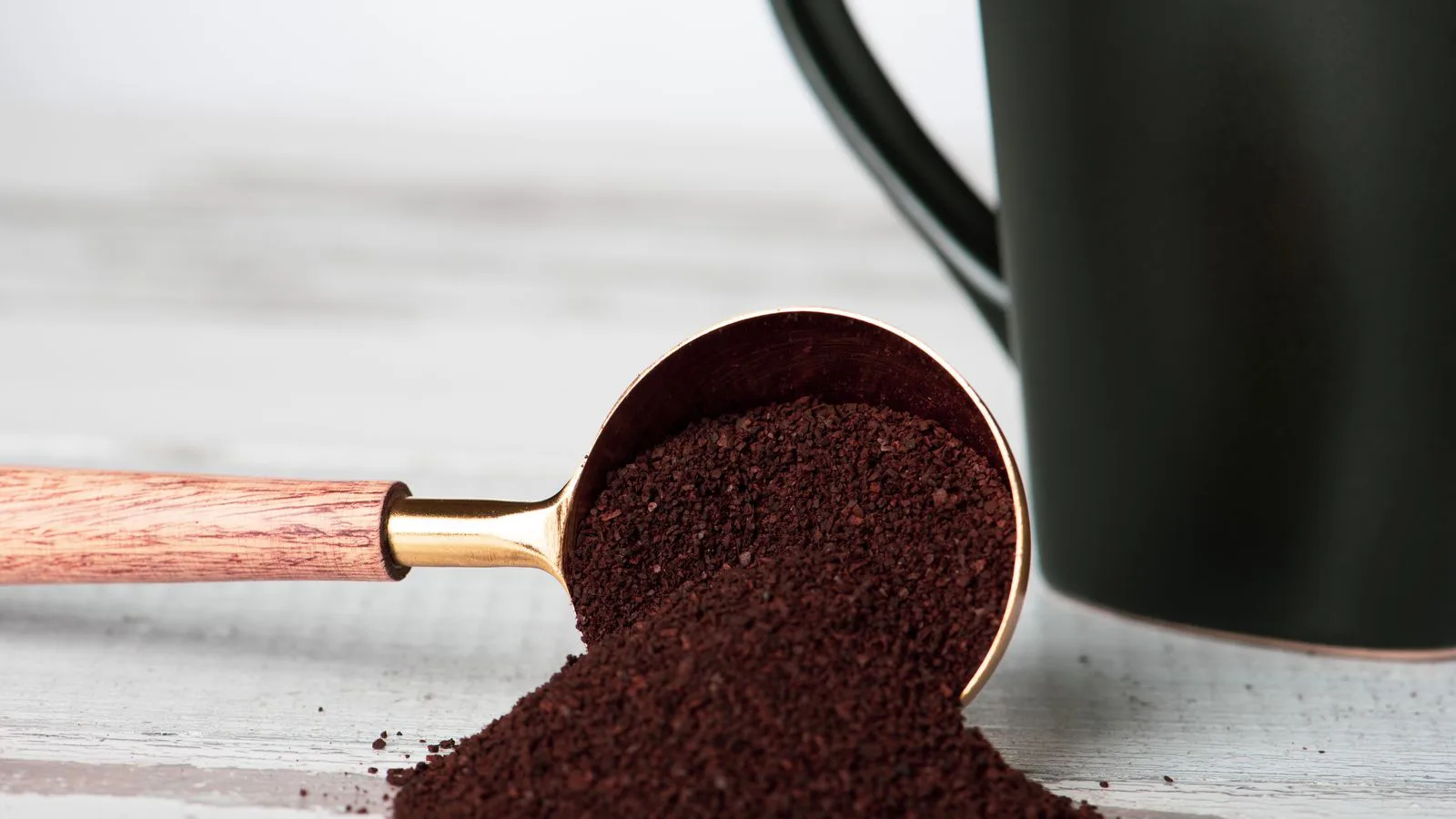 Caffè macinato che cade da un misurino accanto a una brocca.