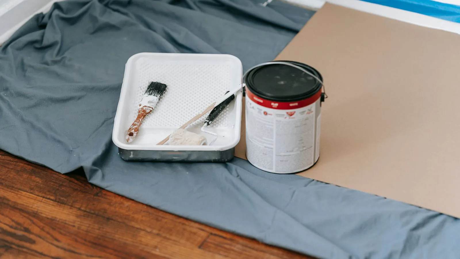 A paint tin, brushes and a dust sheet ready for decorating.