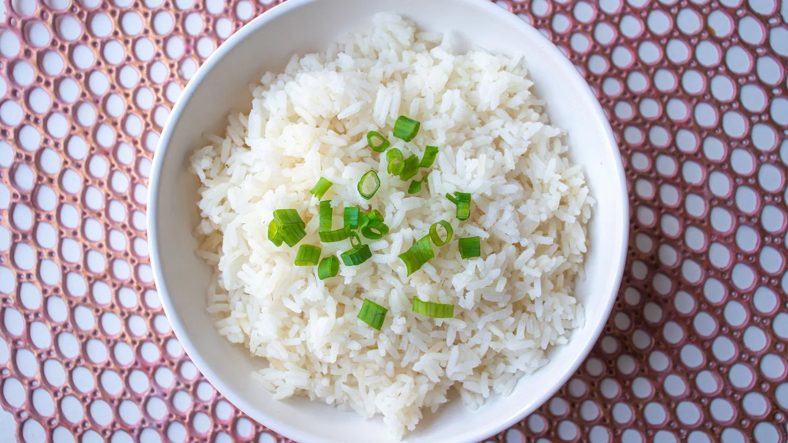A bowl of cooked white rice topped with spring onion.
