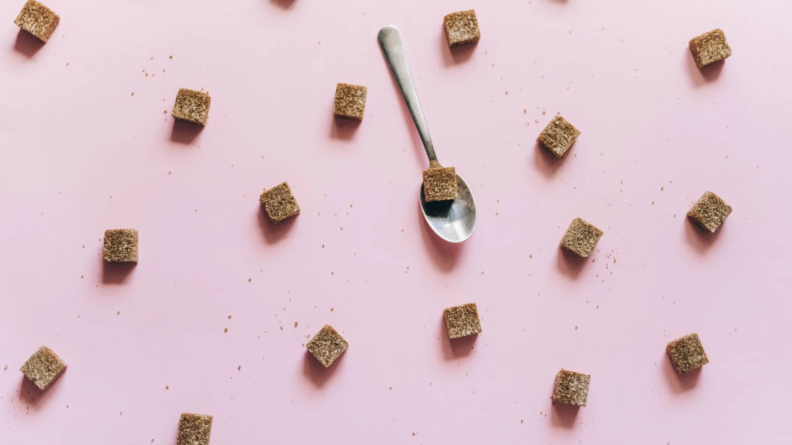 Cubos de açúcar amarelo espalhados sobre um fundo cor-de-rosa, vistos de cima.