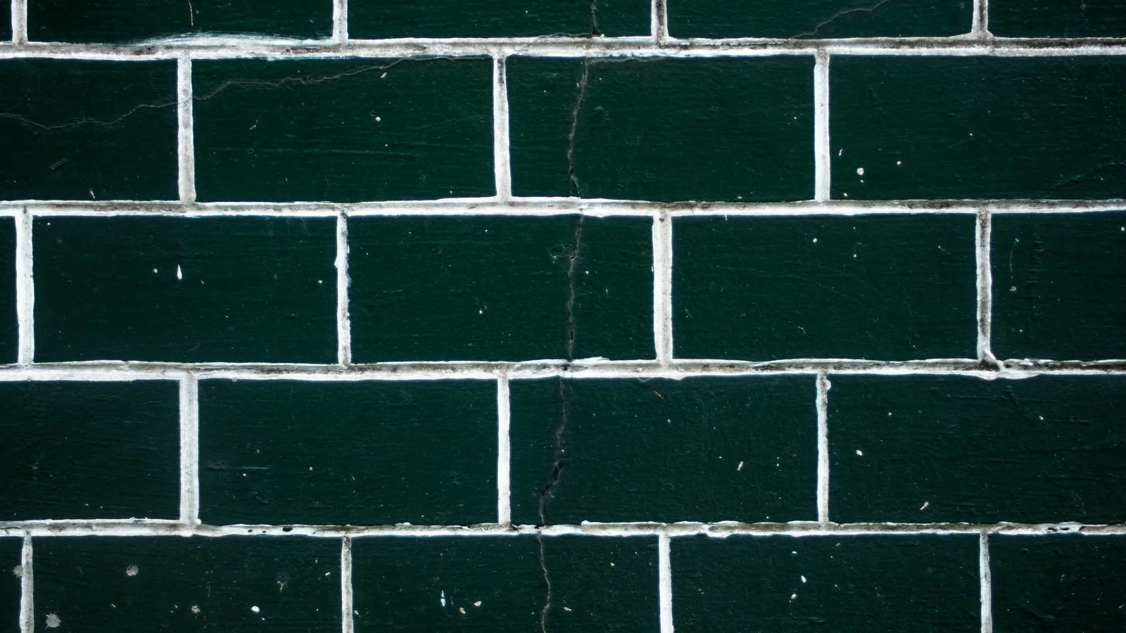 A wall of dark green glazed tiles with the grout lines showing.