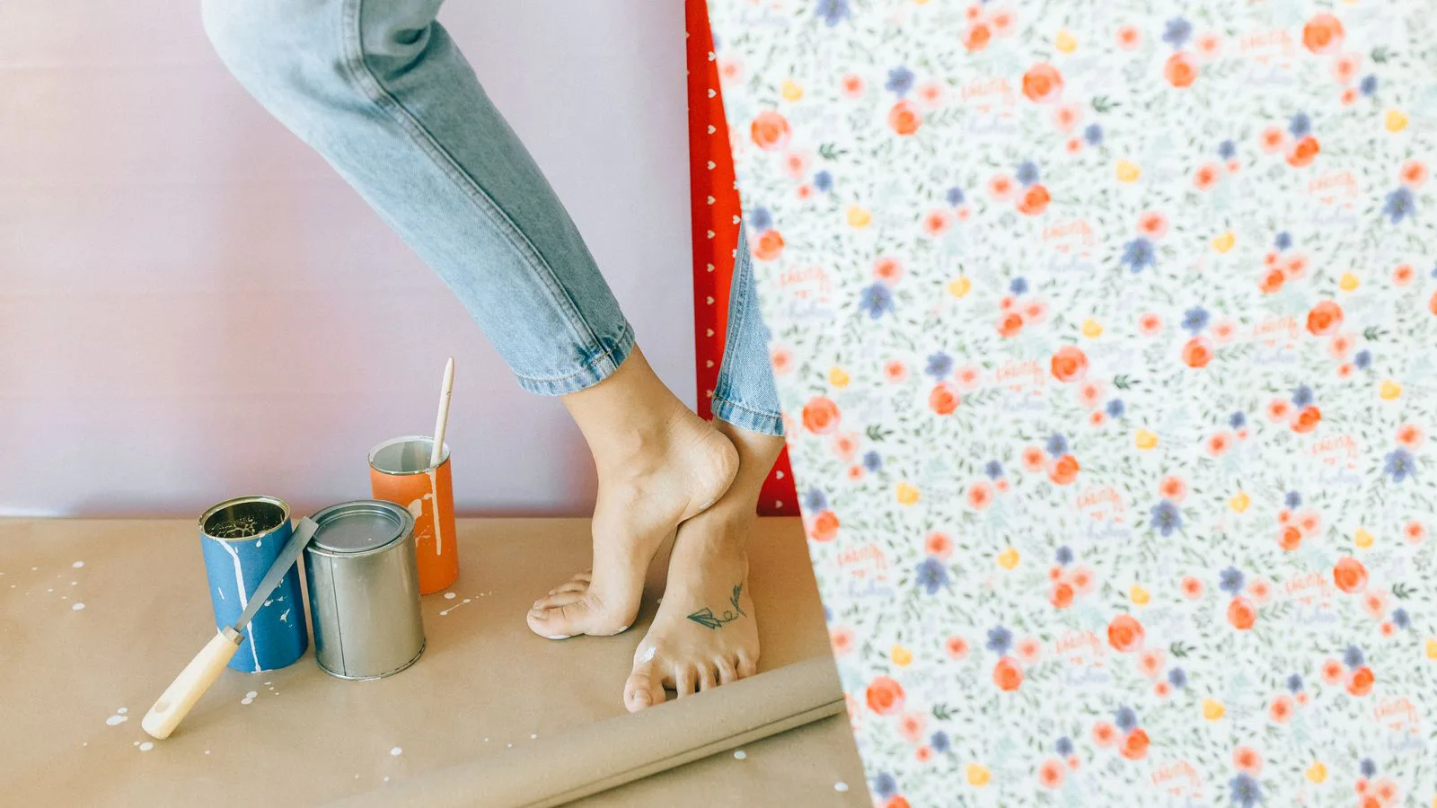 A woman hanging patterned wallpaper, paste tins at her feet.