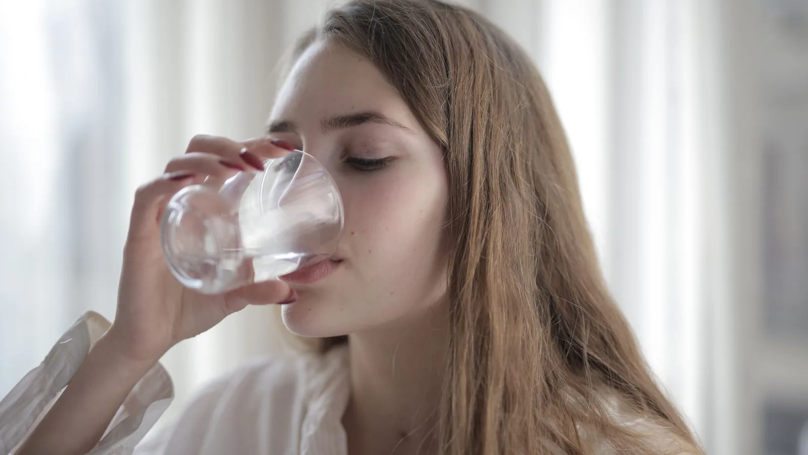 Eine Frau trinkt drinnen ein Glas Wasser.