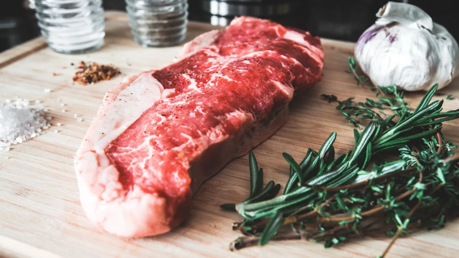 A raw steak on a wooden board with herbs and garlic.