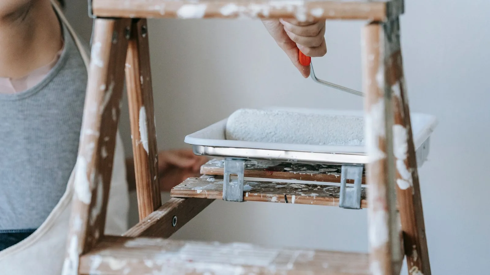 A woman on a stepladder painting a wall with a roller.