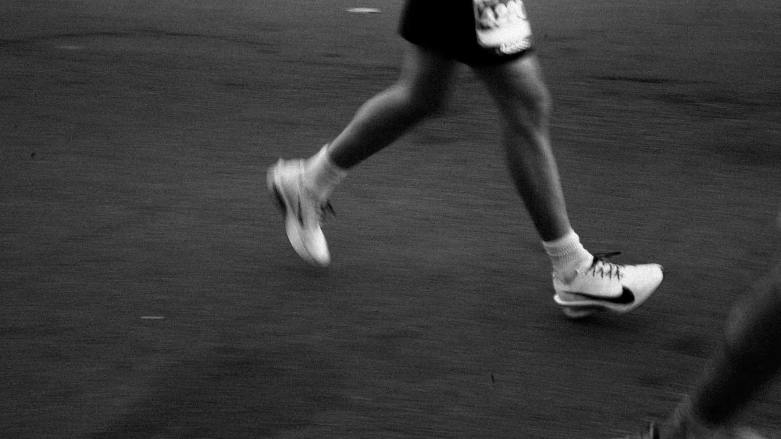 A runner's legs in motion on tarmac, in black and white.