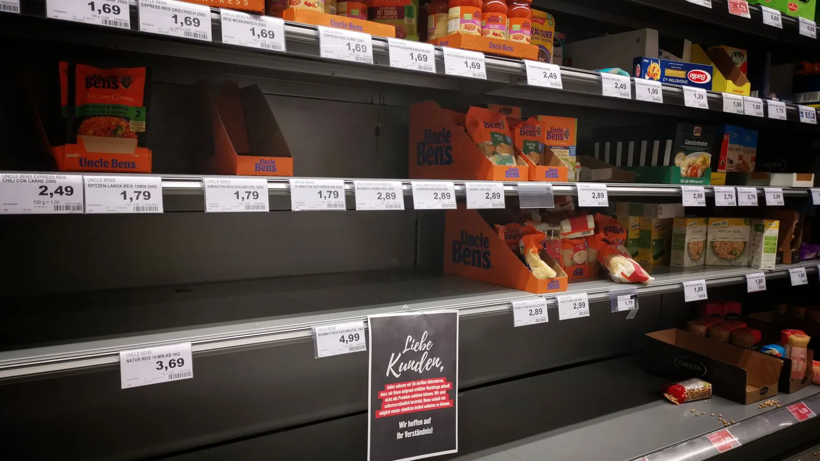 Supermarket shelves of jars and packets with price labels on the edge.