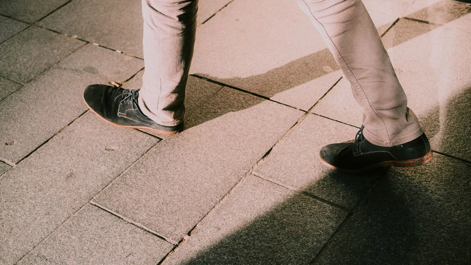 Pernas com sapatos pretos a caminhar sobre um pavimento de pedra.