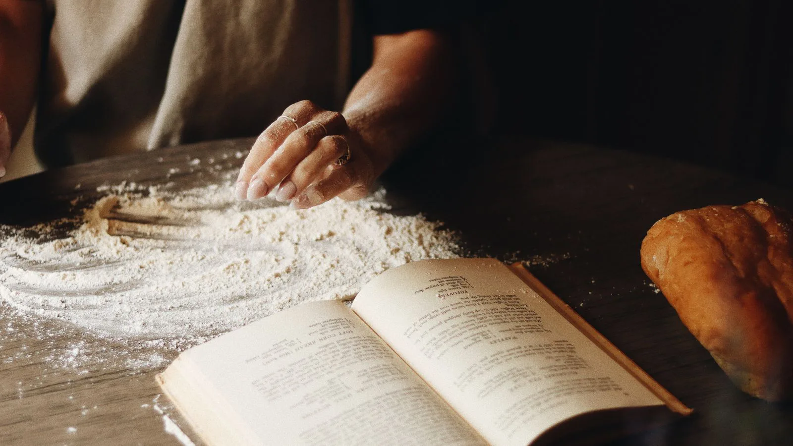 Hands shaping dough beside an open recipe book dusted with flour.