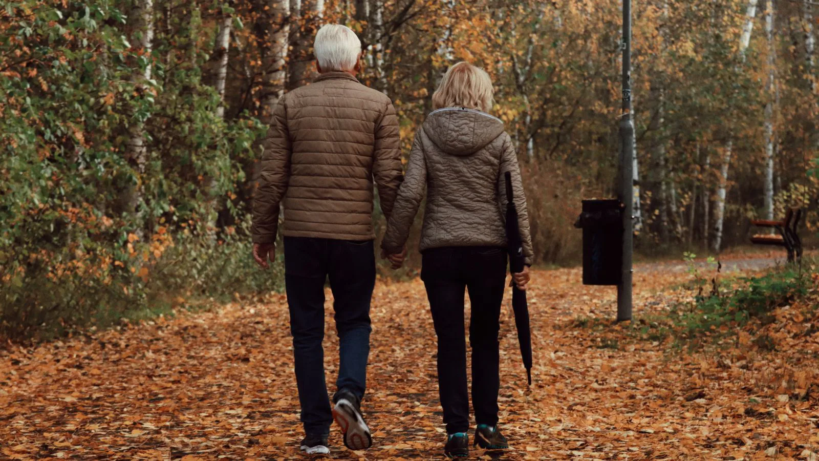 Un couple âgé marche sur un chemin boisé en automne.