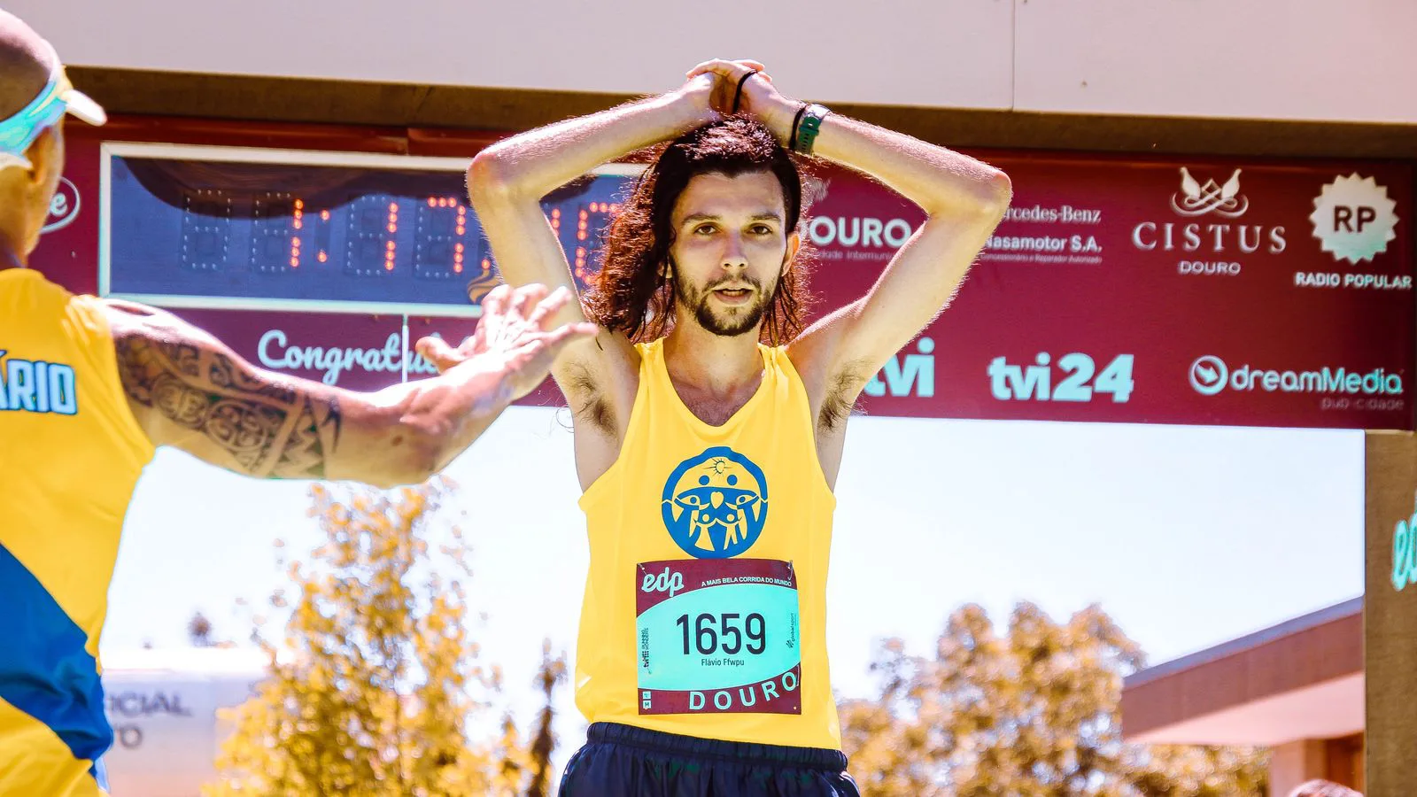 A runner crossing the finish line of a road race, arms raised.