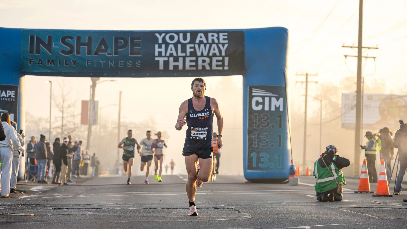 A runner passing the halfway arch of a road race, spectators behind.