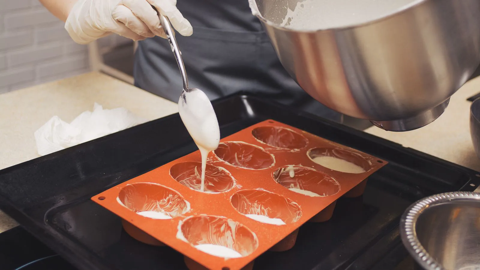 Gloved hands pouring batter into silicone moulds.