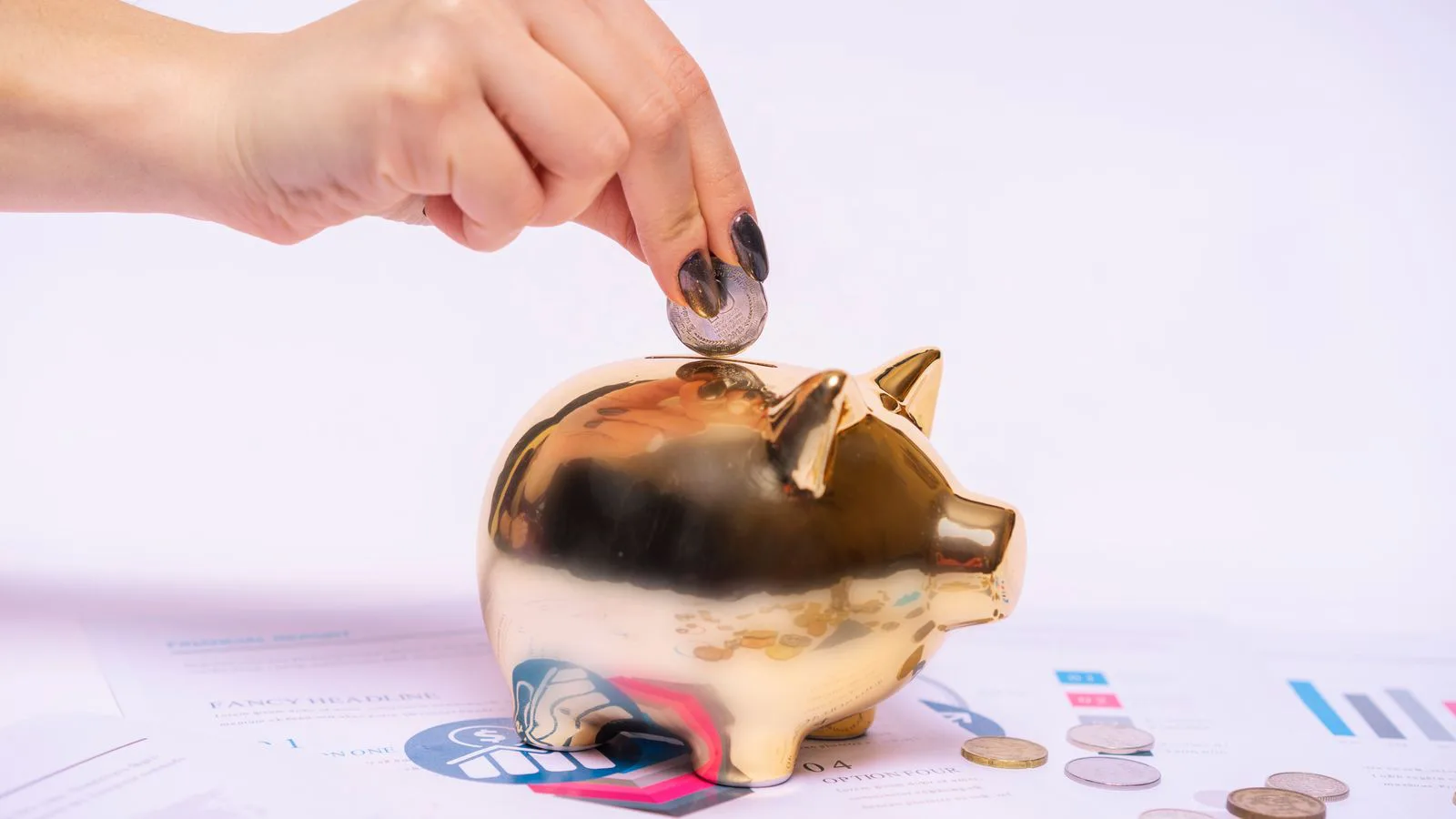 A hand dropping a coin into a piggy bank.