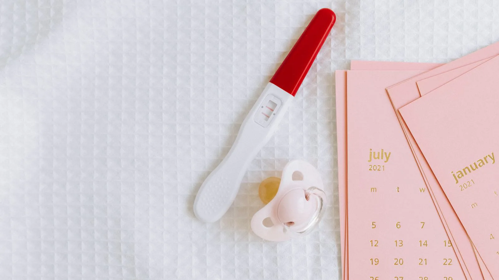 A positive pregnancy test beside a pacifier and a calendar.