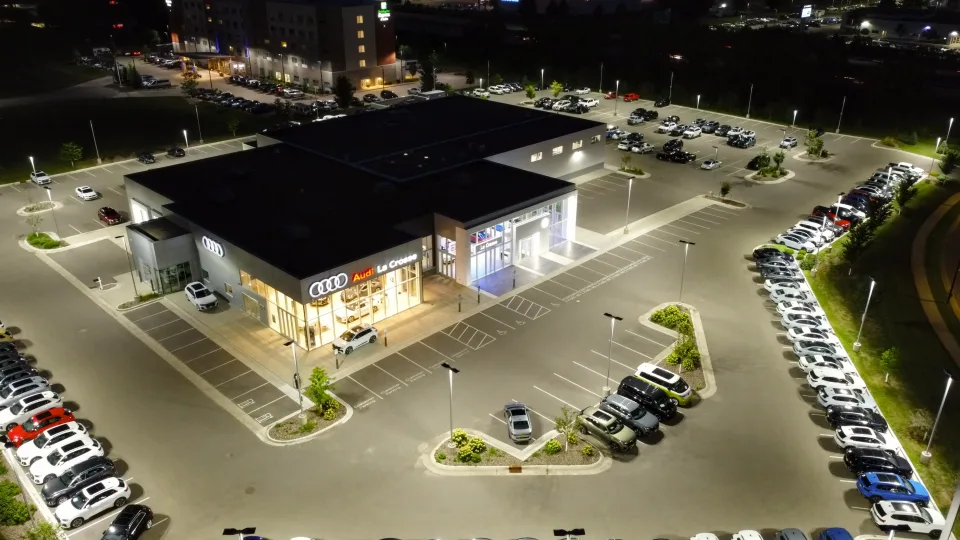 Aerial night view of a car dealership and its lit forecourt full of cars.