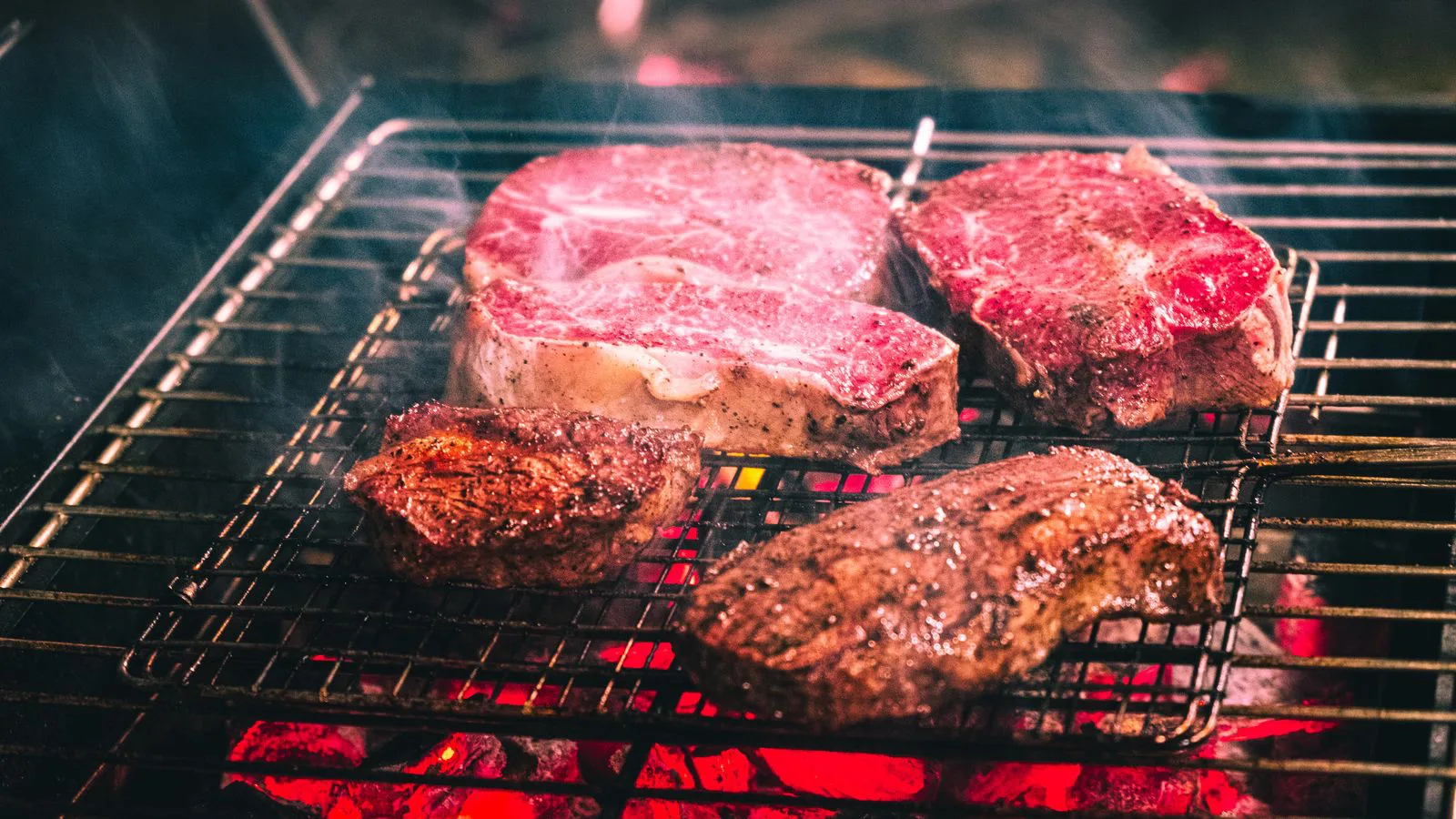 Steaks searing on a barbecue grill over glowing coals.