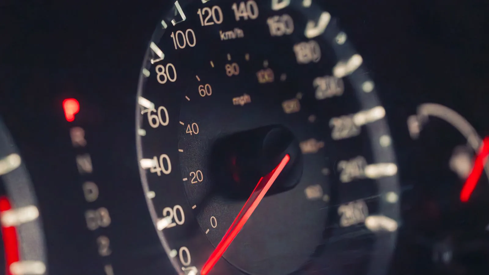 A car speedometer marked in km/h and mph, in low light.