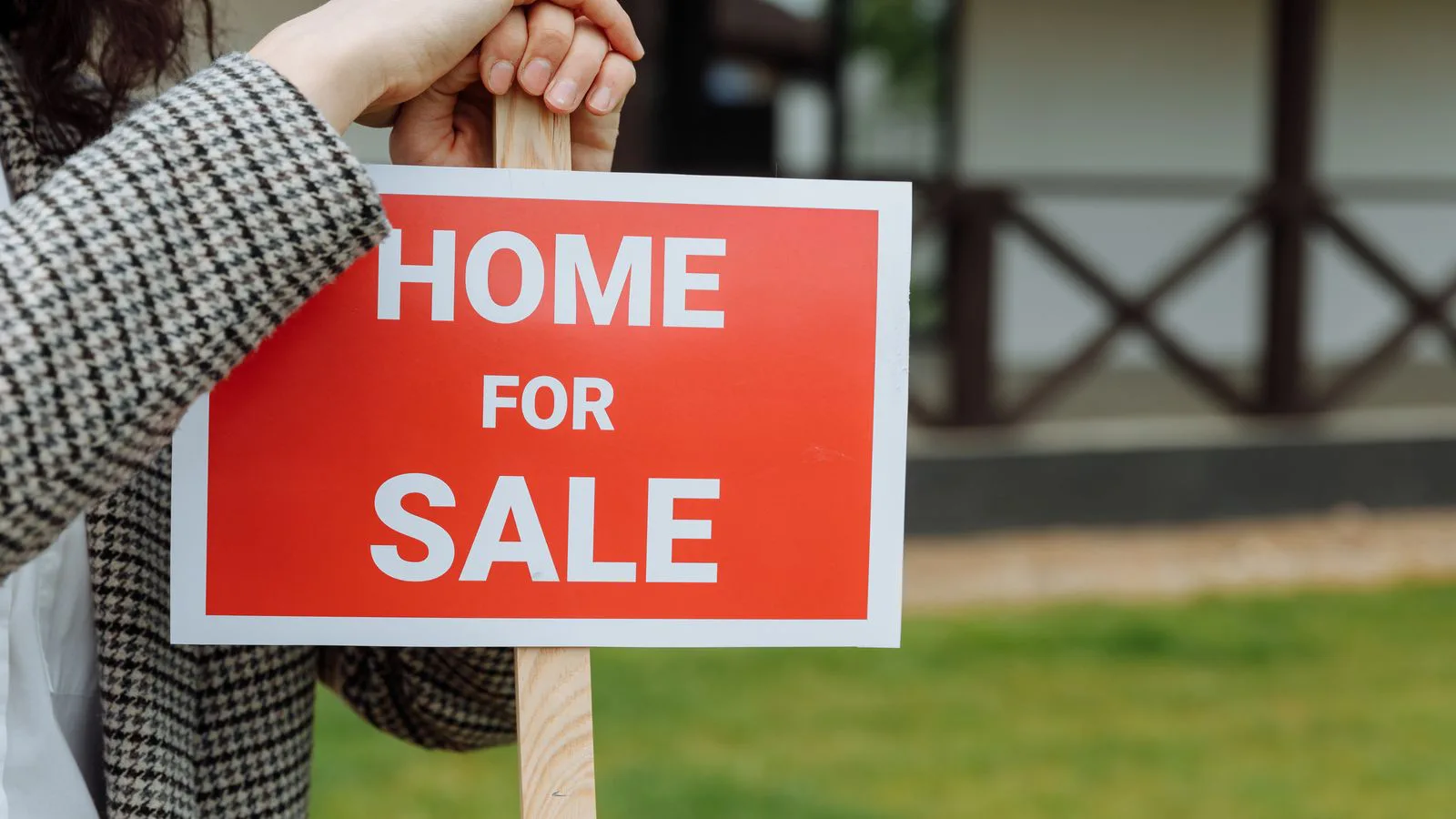 A person holding up a “for sale” board in front of a house.