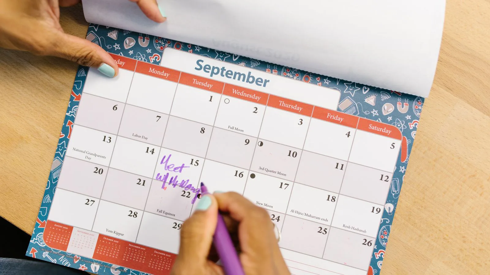 A hand marking a date on a paper calendar.