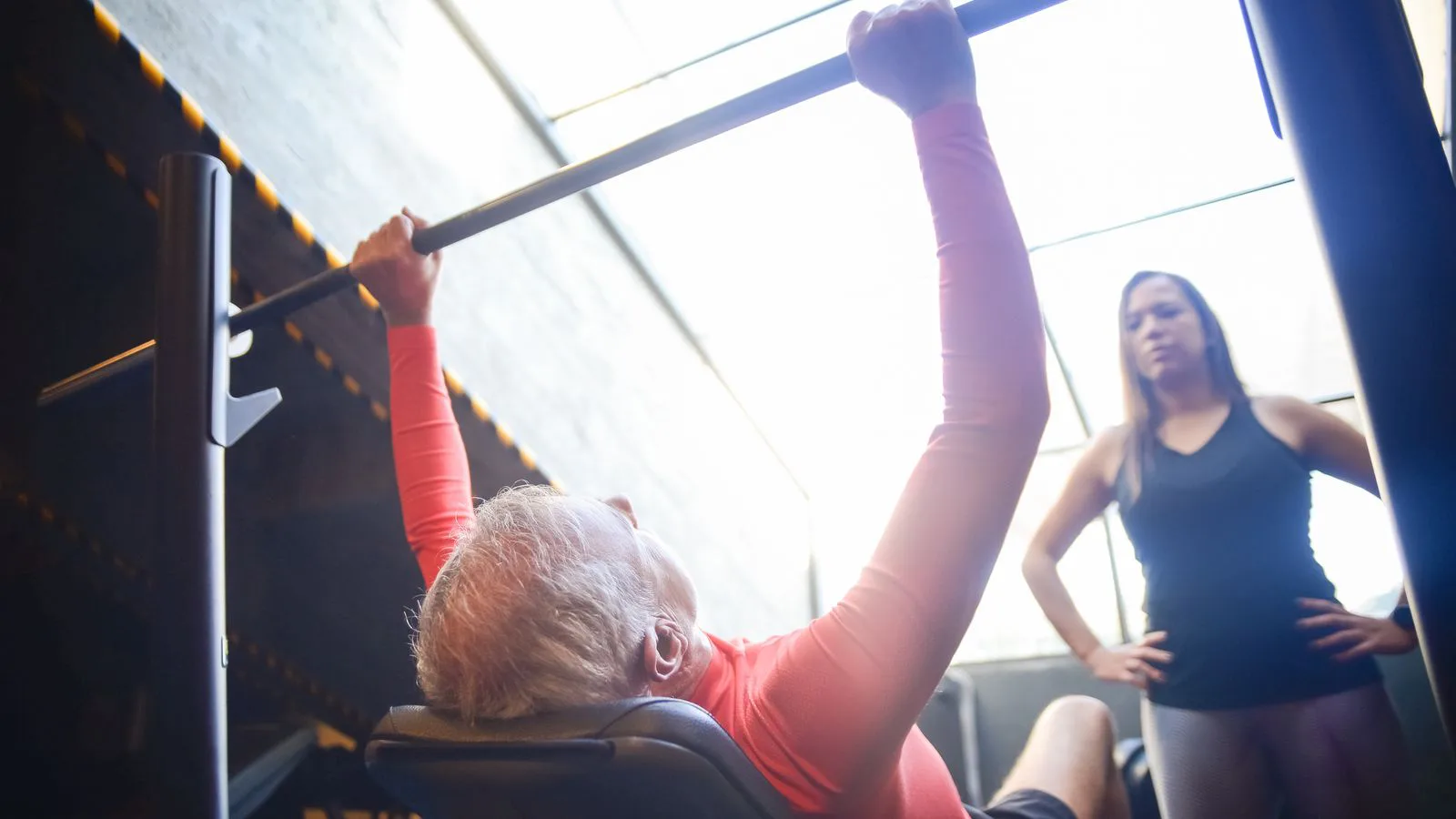 A man bench pressing while a trainer spots the bar.