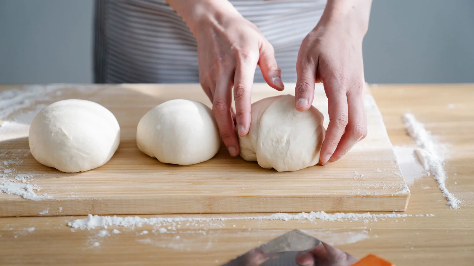 Balls of pizza dough resting on a floured wooden board.