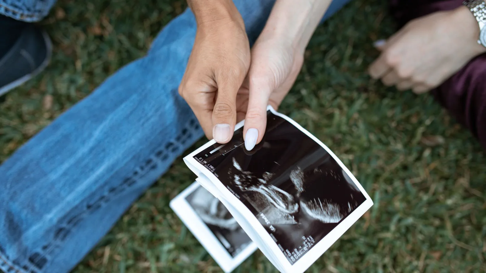 Hands holding an ultrasound image over grass.