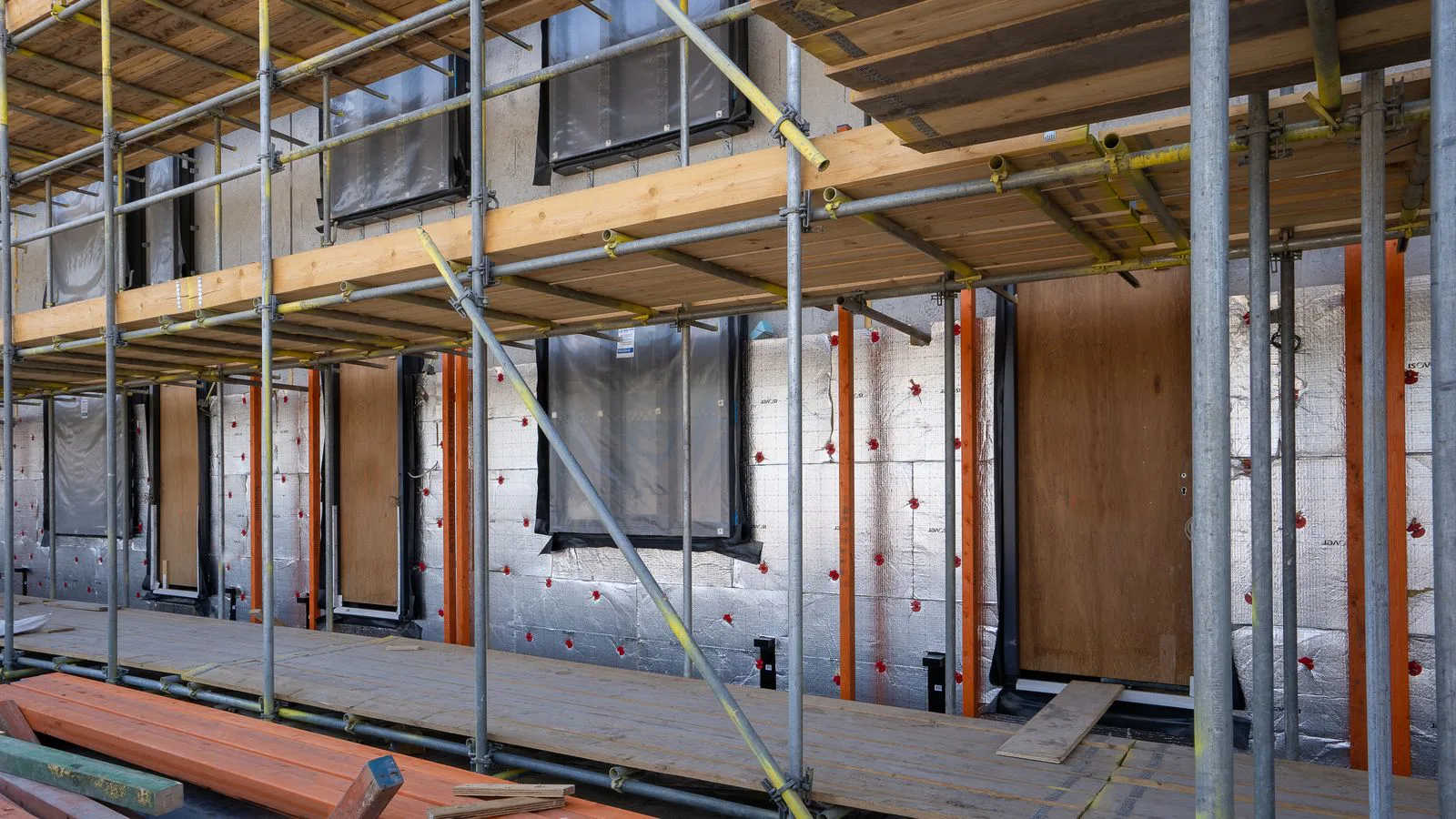 Scaffolding against a house under construction, insulation work in progress.