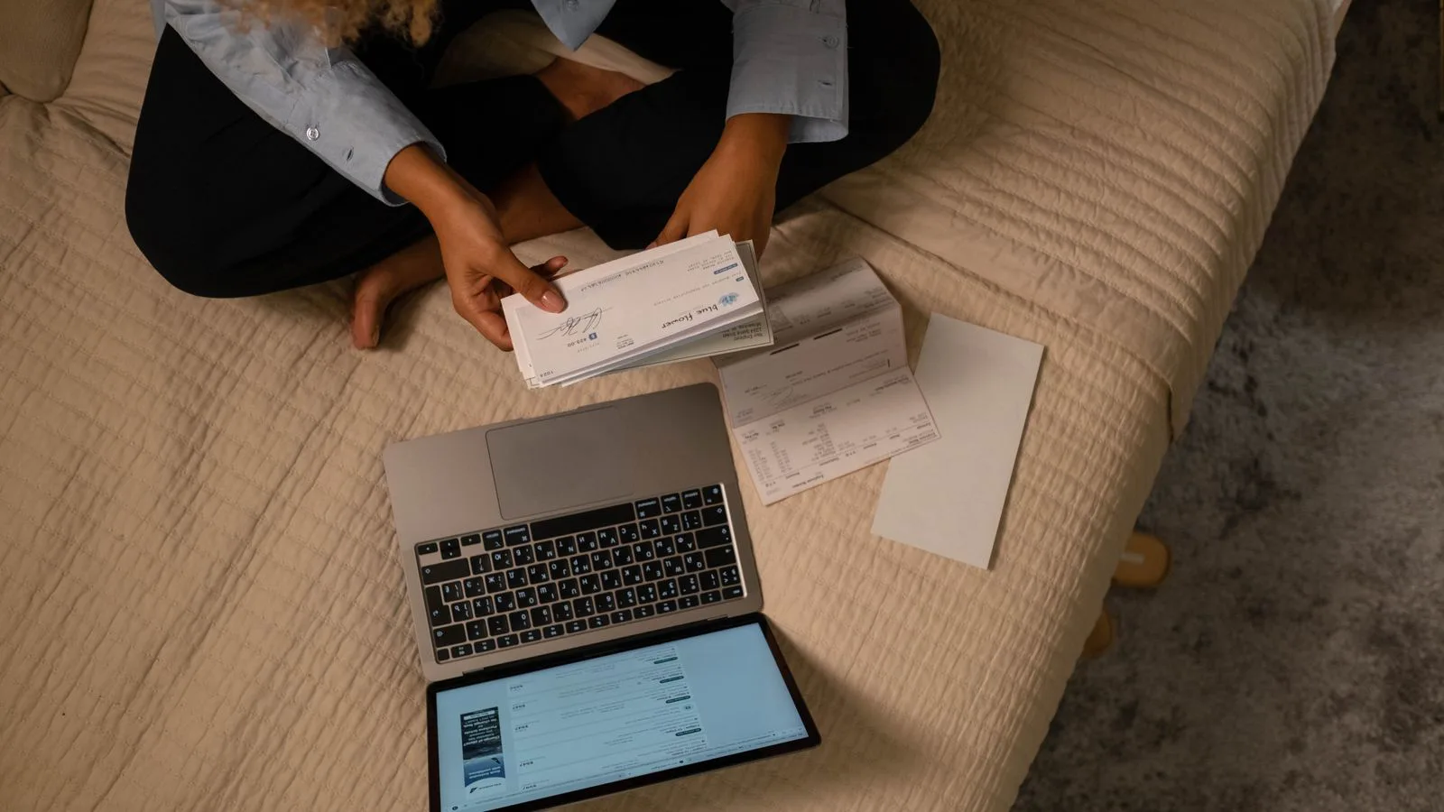 A woman going through bills with a laptop and papers spread out.
